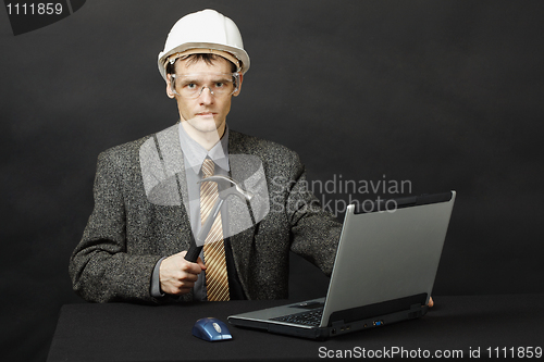 Image of Man in helmet with hammer repairs computer