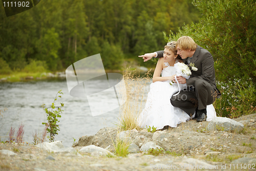 Image of Bride and groom sit on riverbank