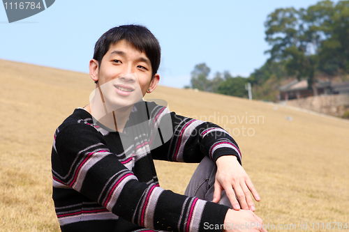Image of handsome forties man is sitting on the grass relaxing and smilin