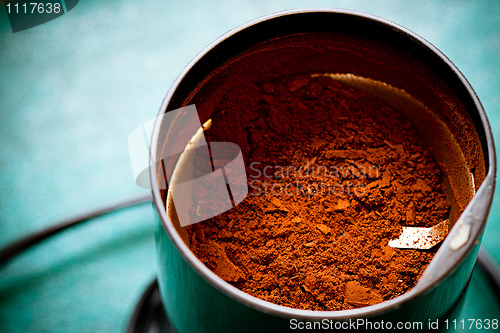 Image of Electrical coffee-mill machine with milled ground coffee on the green tabletop with top cover removed