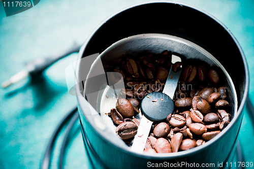 Image of Electrical coffee-mill machine with roasted coffee beans on the green tabletop with top cover removed