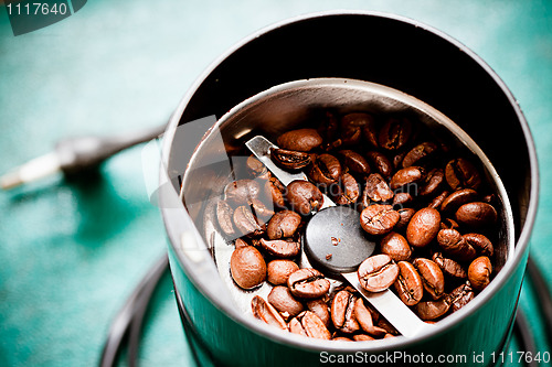 Image of Electrical coffee-mill machine with roasted coffee beans on the green tabletop with top cover removed