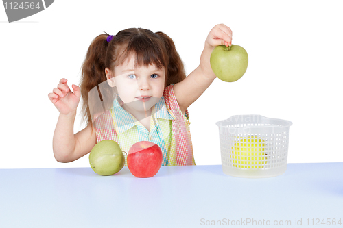 Image of Little girl playing with green apples sitting at table