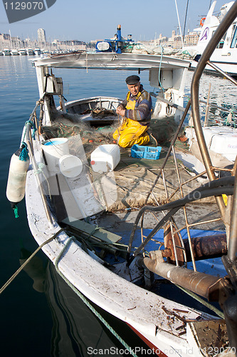 Image of MARSEILLE, FRANCE,  MARCH 6: a fisherman, on the knees in his boat, in the Vieux-Port, tidies up his nets, on Sunday, March 6th, 2011 in Marseille, France.