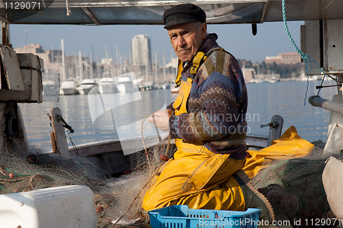 Image of MARSEILLE, FRANCE,  MARCH 6: a fisherman, on the knees in his boat, in the Vieux-Port, tidies up his nets, on Sunday, March 6th, 2011 in Marseille, France.