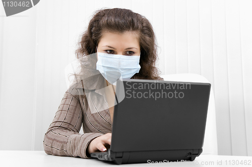 Image of The young woman in medical mask with the laptop