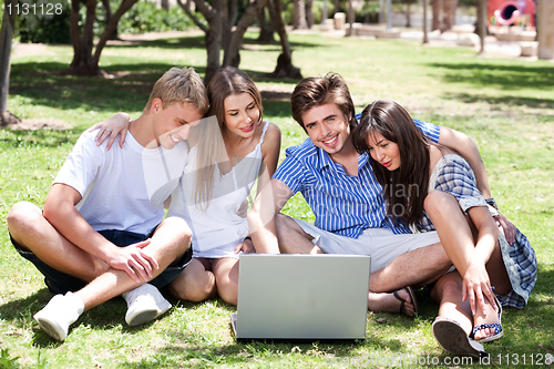Image of Friends enjoying movie in park on laptop
