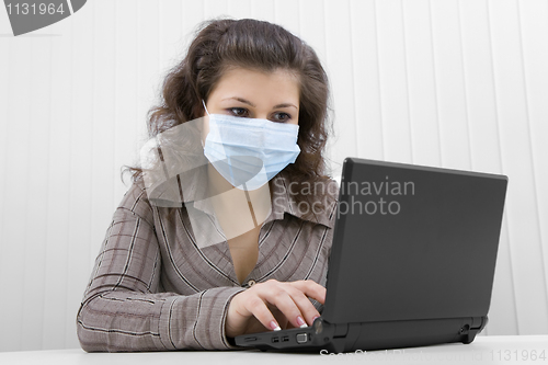 Image of The young woman in medical mask with the laptop