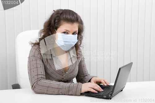 Image of The young woman in medical mask with the laptop