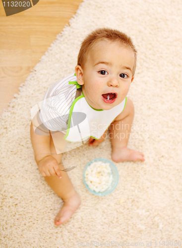Image of Baby boy sitting on carpet and eating alone