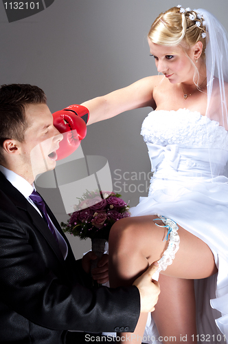 Image of Young bride hitting groom while he takes off wedding garter