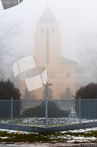 Image of Church in the fog with stone cross and fence