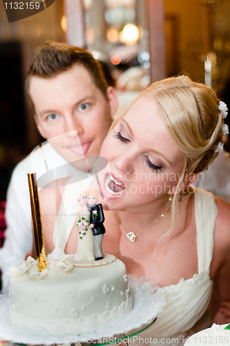 Image of Young bride is going to bite her cake with groom in background