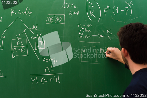 Image of Young student writing formulas on green chalk board