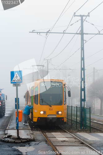 Image of New tram with passanger getting on in the fog