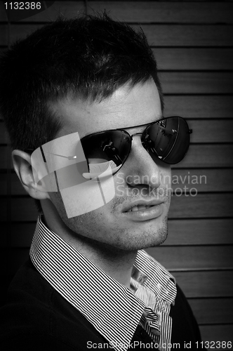 Image of Close-up of a young man in sunglasses against blinds in black an