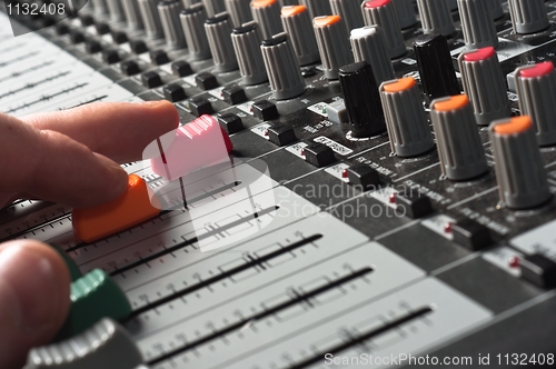 Image of Part of an audio sound mixer with buttons and sliders and hand