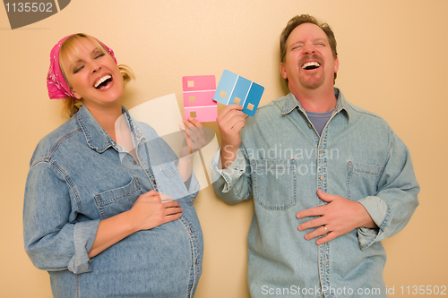 Image of Pregnant Laughing Couple Deciding on Pink of Blue Wall Paint
