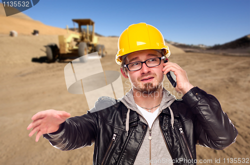 Image of Young Cunstruction Worker on Cell Phone in Dirt Field with Tract