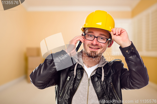 Image of Young Contractor Wearing Hard Hat on Cell Phone In House