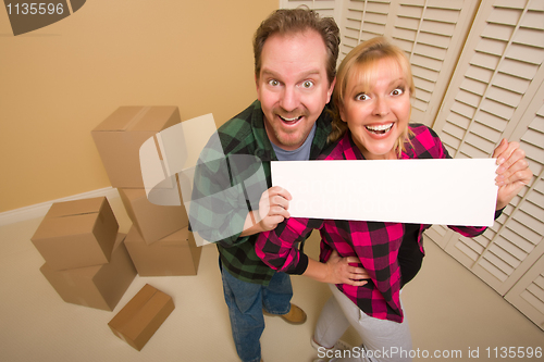 Image of Happy Couple Holding Blank Sign in Room with Packed Boxes