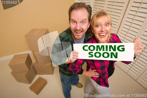 Image of Goofy Couple Holding Coming Soon Sign in Room with Boxes