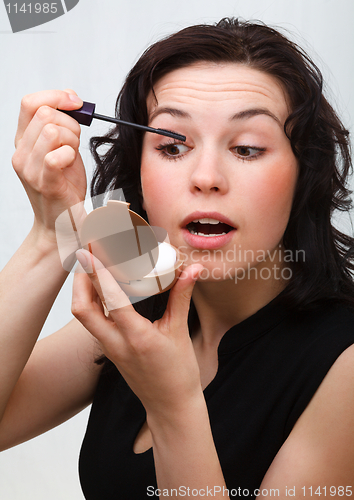 Image of Woman is applying mascara while looking in mirror