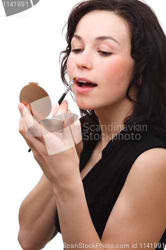 Image of Woman is applying lipgloss while looking in mirror