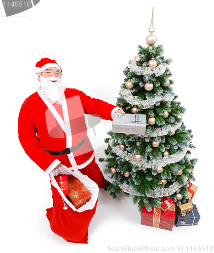 Image of Santa Claus offering present in front of Christmas tree