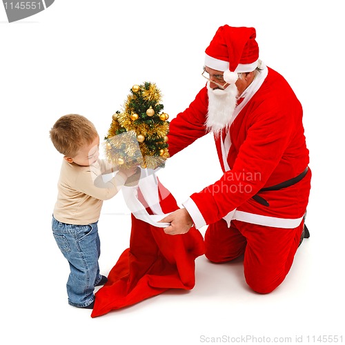 Image of Little boy puts small tree in Santa's bag