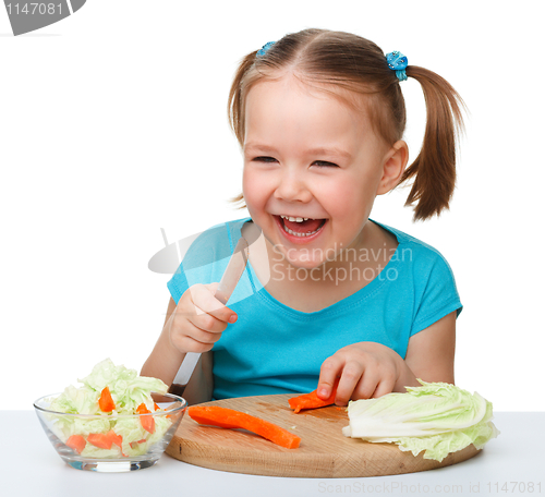 Image of Little girl is cutting carrot for salad