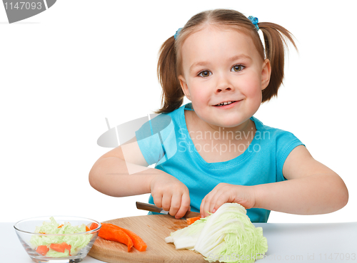 Image of Little girl is cutting carrot for salad