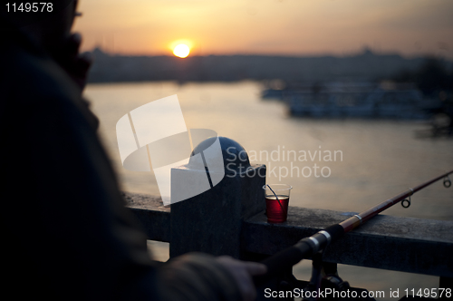 Image of Man fishing from bridge in sunset