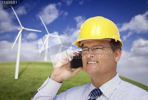 Image of Hard Hat Wearing Engineer on Phone with Turbines Behind