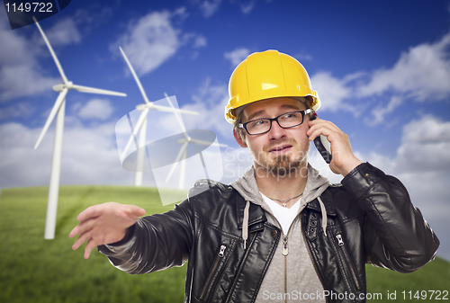 Image of Hard Hat Wearing Engineer on Phone with Turbines Behind