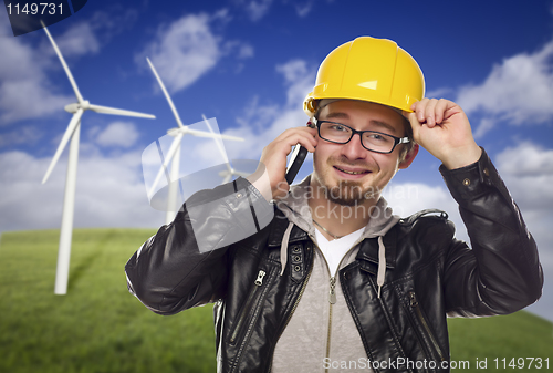 Image of Hard Hat Wearing Engineer on Phone with Turbines Behind