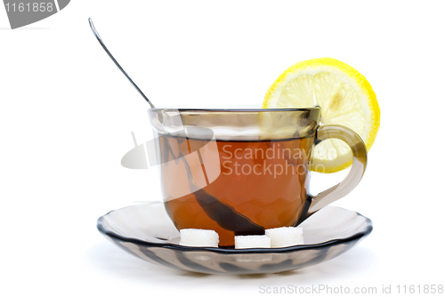 Image of Teacup with black tea, teaspoon, dish, lemon slice and some sugar pieces