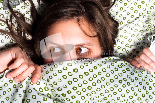 Image of Young scared girl hiding under blanket