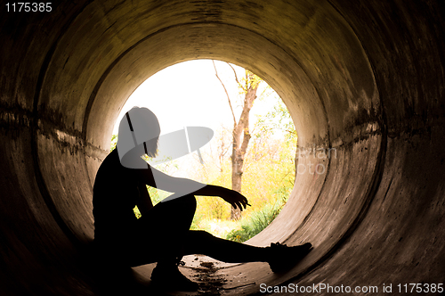 Image of Silhouette of a young girl smoking in sewer pipe