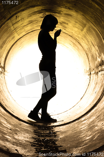 Image of Silhouette of a young girl smoking in sewer pipe