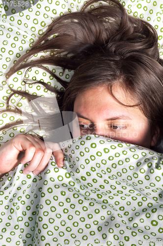 Image of Young scared girl hiding under blanket