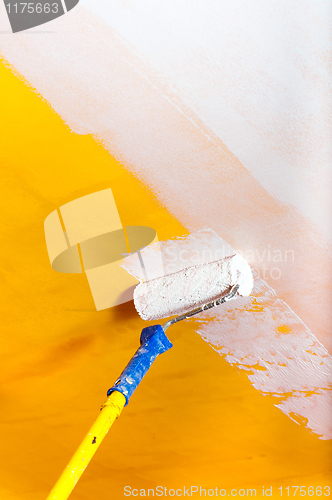 Image of White paint over yellow wall with painting rod