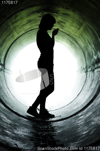 Image of Silhouette of a young girl smoking in sewer pipe