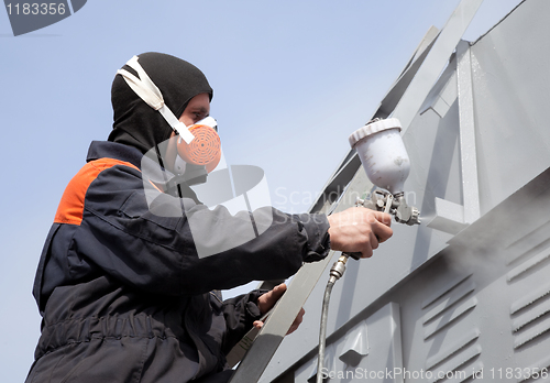 Image of A commercial painter on the stairs spray painting a steel exteri