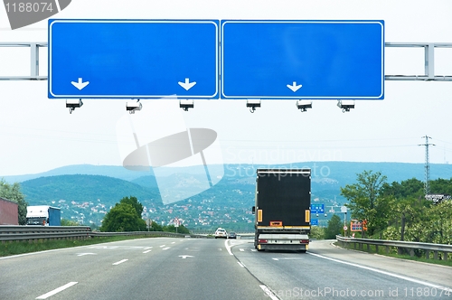 Image of Big blue sign on highway with truck and car