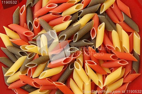 Image of penne tricolore pasta on red background
