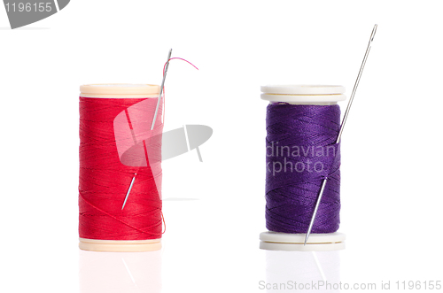Image of Two red and purple thread bobbin and needle 
