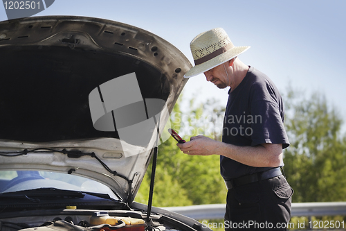 Image of man on a mobile phone in front of a broken car