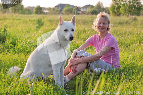 Image of The woman with a dog sit on a meadow