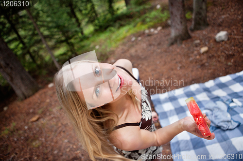 Image of Blond woman eating watermelon while picnic